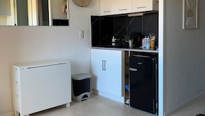 Une cuisine de taille réduite avec des meubles blancs, un réfrigérateur noir et une petite poubelle.