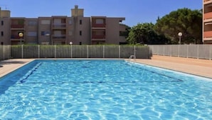 Une piscine rectangulaire à l’eau d’un bleu limpide, entourée d’une clôture et bordée, au fond, d’un bâtiment doté de balcons.