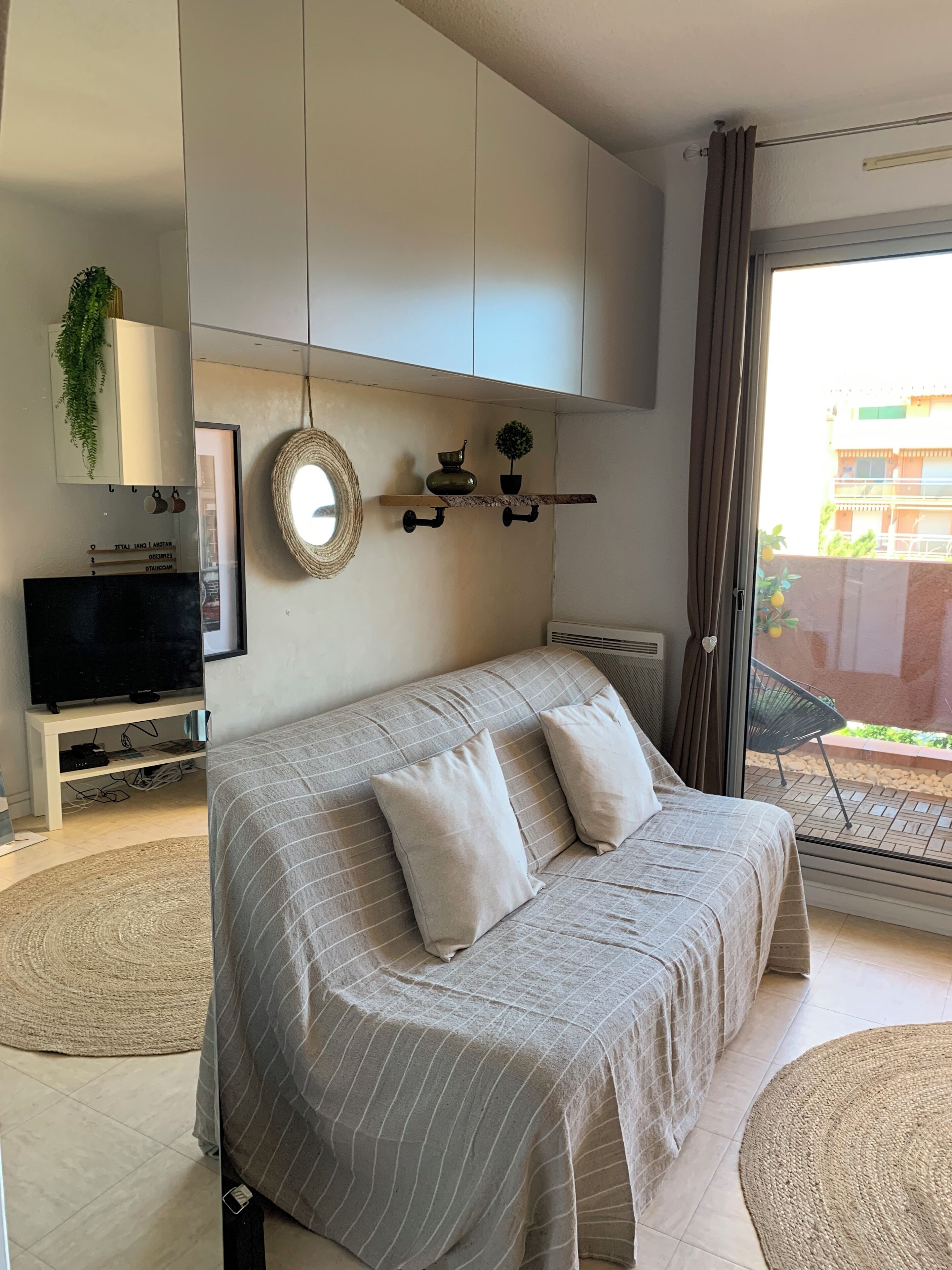 A modern bedroom with a large bed, a TV, a shelf with decorative items, and a view of the outside.