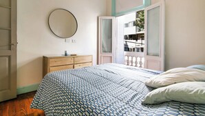 Un dormitorio con cama, cómoda, espejo y ventana con vista a un balcón.