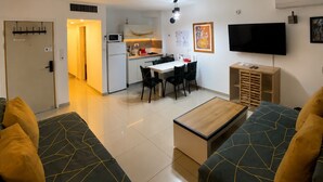 Un salon moderne comprenant un canapé, une table basse, un téléviseur et un coin cuisine avec un four à micro-ondes et une table à manger.
