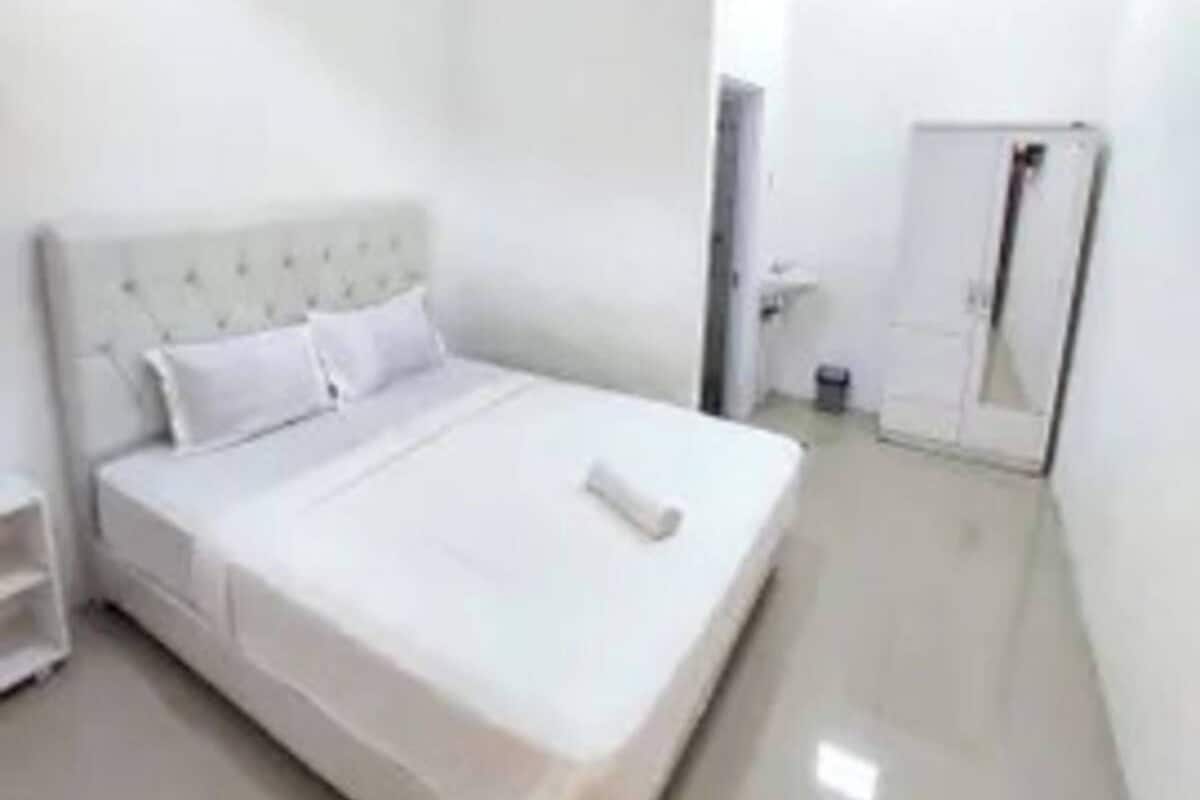 A clean, white hotel room with a single bed, a wardrobe, and a mirror.