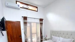 A bedroom with a large bed, a wooden door, and a window with curtains. - Sandi Guest House Syariah (Banyuwangi)
