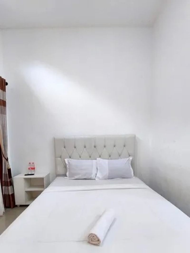 Een hotelkamer met een net opgemaakt bed, een klein nachtkastje met een fles en een effen witte muur.