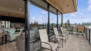 A modern living area with a kitchen, large windows, and a balcony with seating. - New Build, Pool, 1 bed 1 bath Condo at the Quarry (Whitefish)