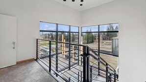 A spacious room with large windows, a metal railing, and a door. - New Build, Pool, 1 bed 1 bath Condo at the Quarry (Whitefish)