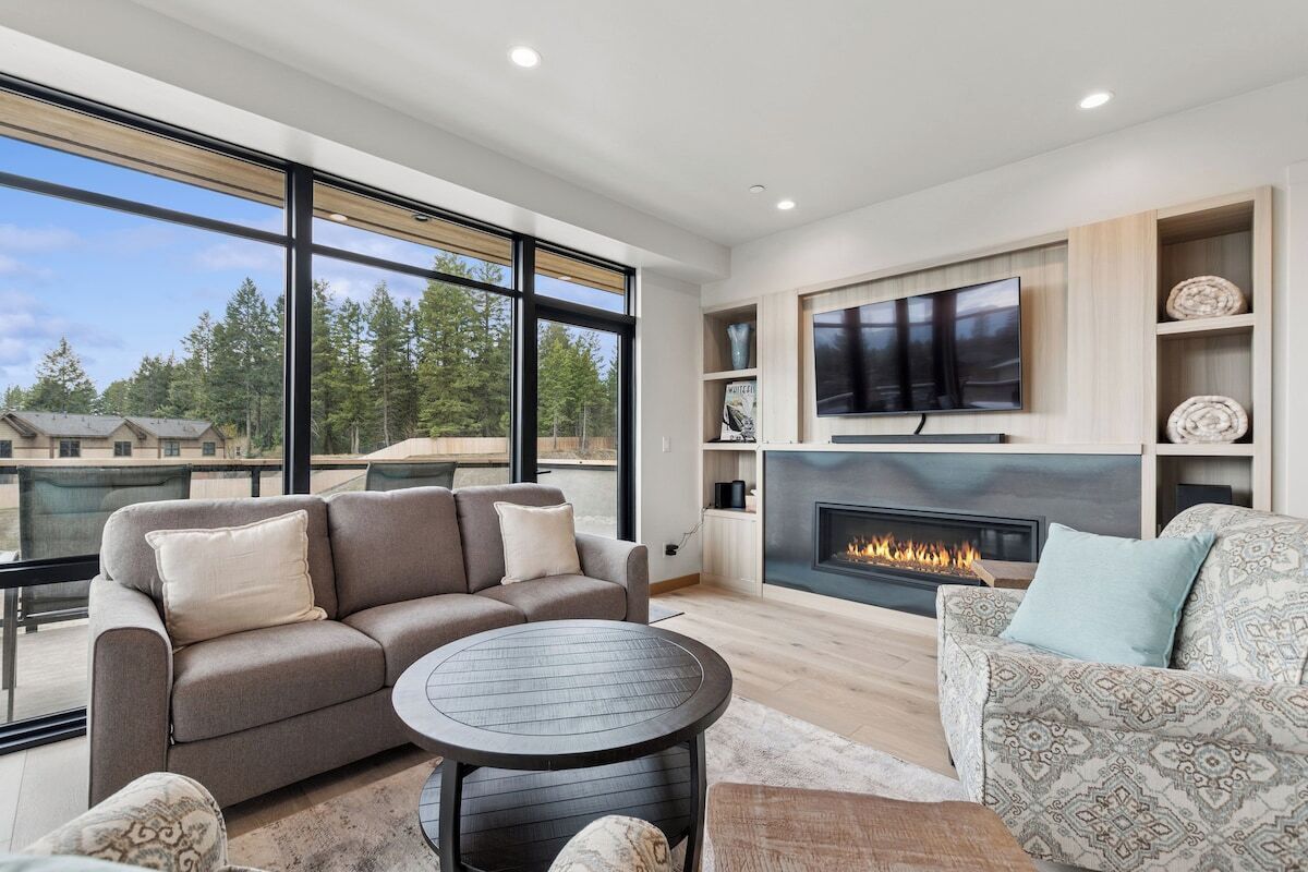 A modern living room with a fireplace, large windows, and a flat-screen TV.