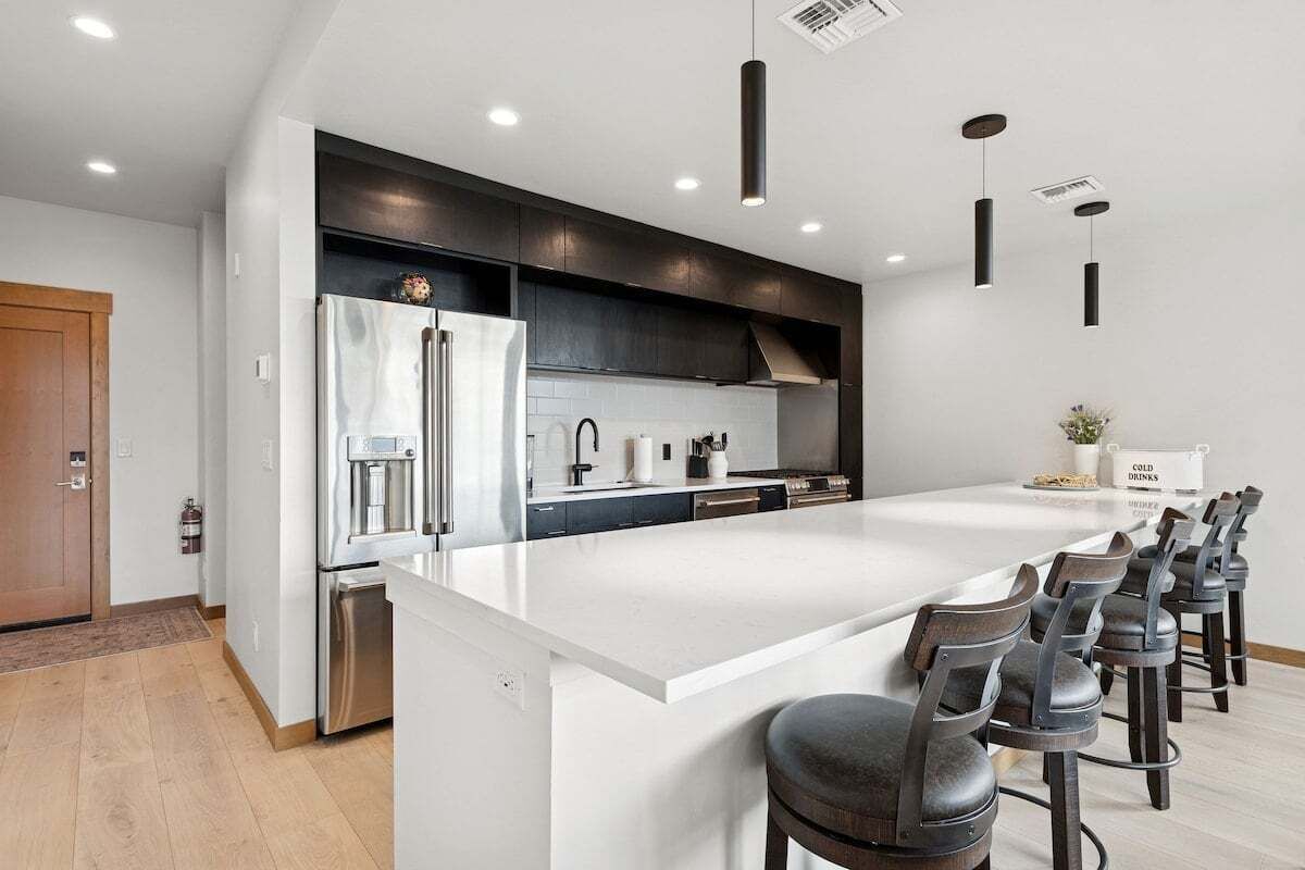 A modern kitchen with a large island, stainless steel appliances, and dark cabinetry.