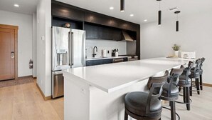 A modern kitchen with a large island, stainless steel appliances, and dark cabinetry. - New Build, Pool, 1 bed 1 bath Condo at the Quarry (Whitefish)
