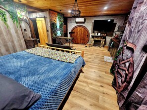 Ein Schlafzimmer mit Bett, Holzboden, Steinwand, Fernseher, Kamin und einer Tür mit Baummalerei.