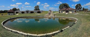 Eine historische Stätte mit einem zentralen Teich, Steinbauten und einem kleinen Gebäude mit rotem Dach.