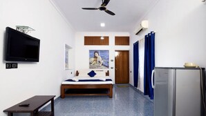 Ein Schlafzimmer mit einem Bett, einem Fernseher, einem Deckenventilator, einem Kühlschrank und einem Fenster mit Vorhängen.