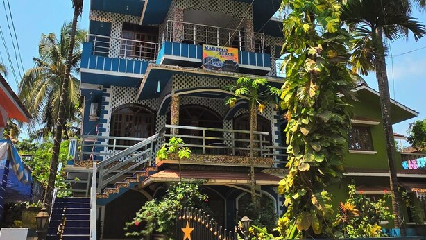 A multi-story building with a balcony, palm trees, and a gate with a star decoration. - Marcelo Palace (Calangute)