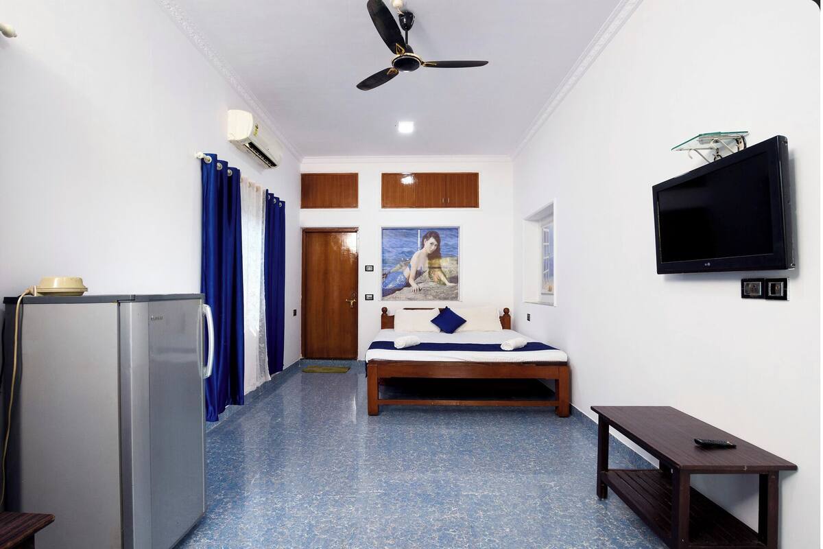 A bedroom with a bed, a TV, a ceiling fan, and a small table.