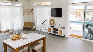 Ett rymligt vardagsrum med ett marmorbord, en tv och ett stort fönster med utsikt över en pool.