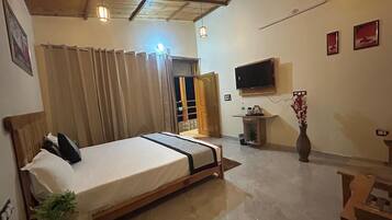 A bedroom with a bed, curtains, a TV, a vase with flowers, and a small table.