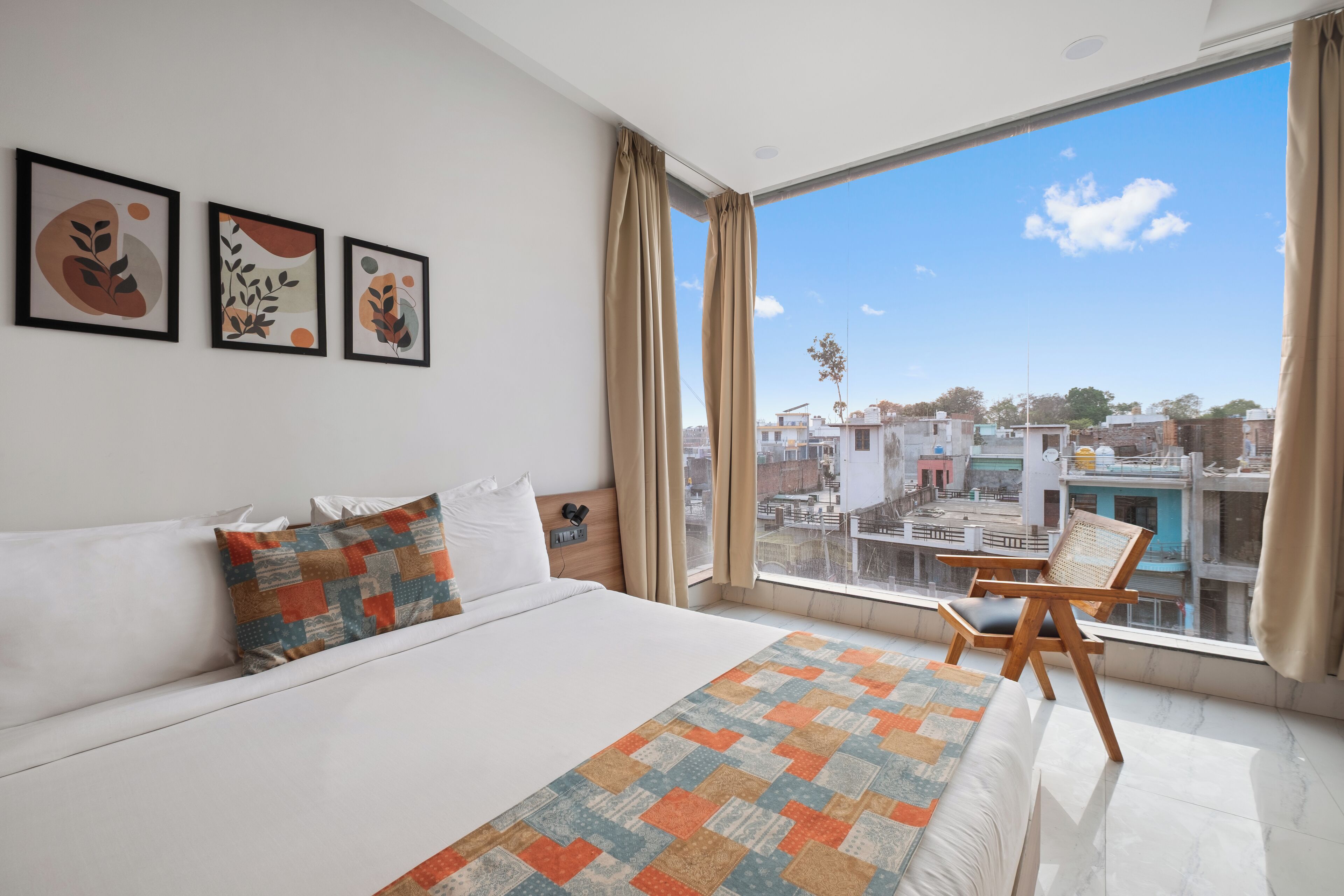 Ein modernes Schlafzimmer mit einem großen Bett, Blick auf die Stadt und drei gerahmten Kunstwerken an der Wand.