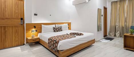 Habitación de hotel moderna con una cama de madera, ropa de cama blanca, una mesita de noche con lámpara, aire acondicionado instalado en la pared y vistas al exterior a través de cortinas.