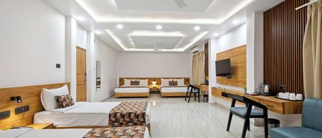A modern hotel room with two single beds, a desk, a chair, a sofa, a ceiling fan, recessed lighting, and a wooden accent wall.