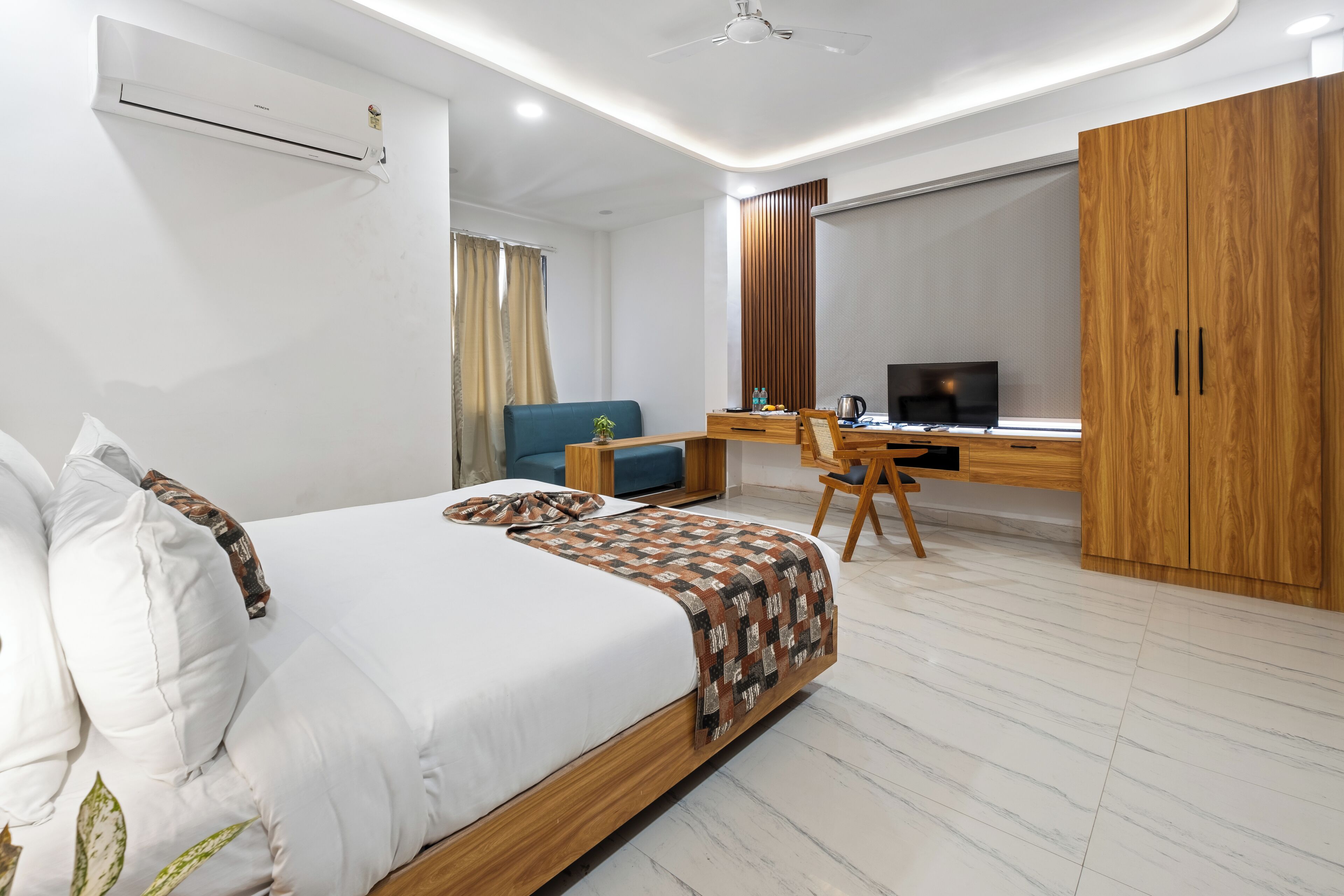 Una habitación de hotel moderna con una cama grande, un escritorio con computadora, un armario y una ventana con cortinas.