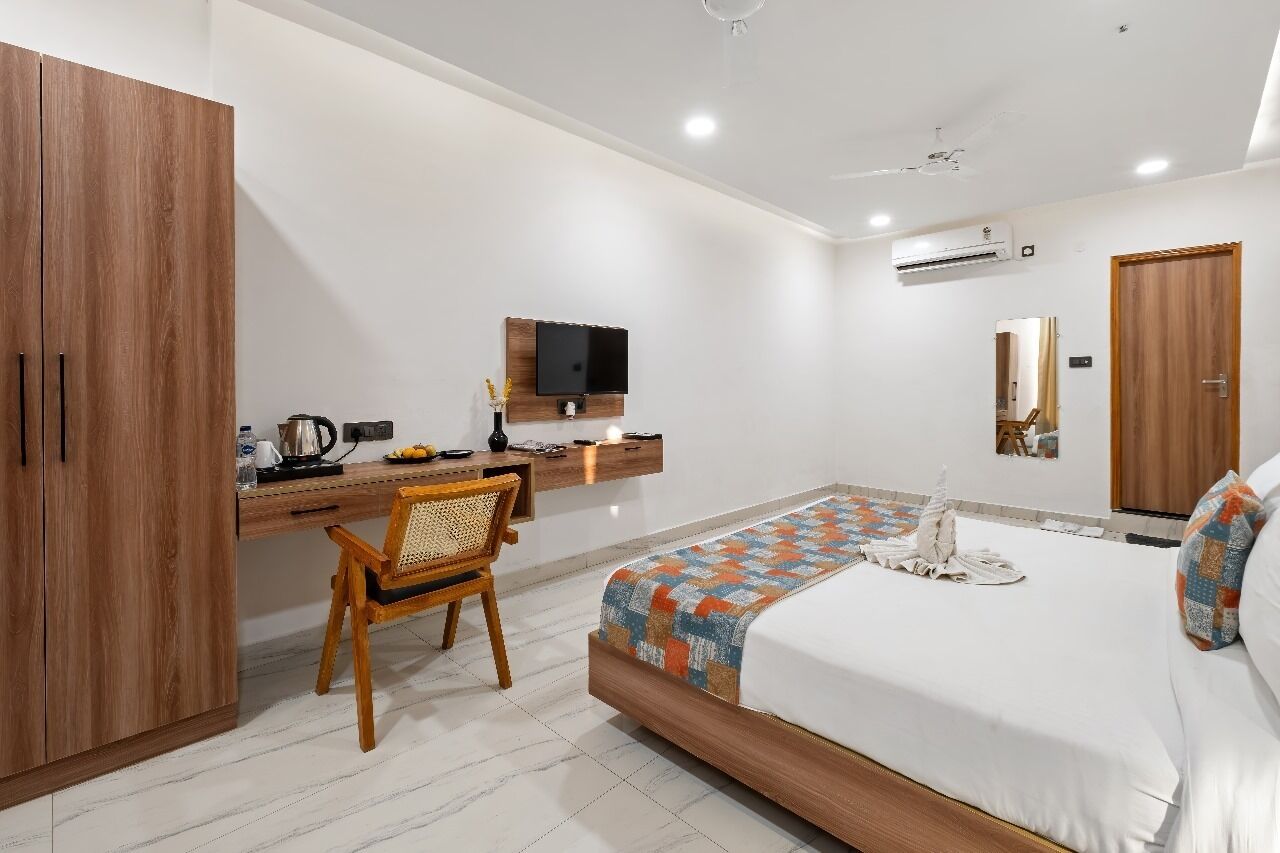 Una habitación de hotel moderna con un armario de madera, un escritorio con televisor de pantalla plana, una cama con colcha colorida y un espejo grande.