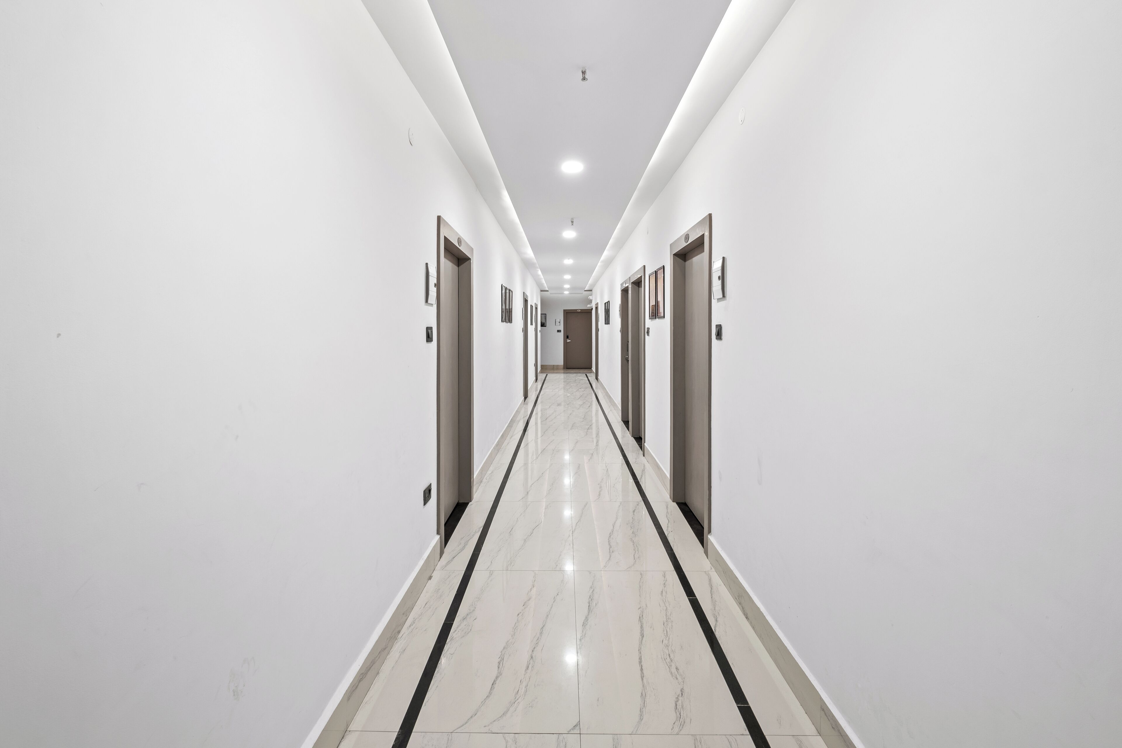 A long, narrow hallway with white walls and a marble floor, leading to a door at the end.