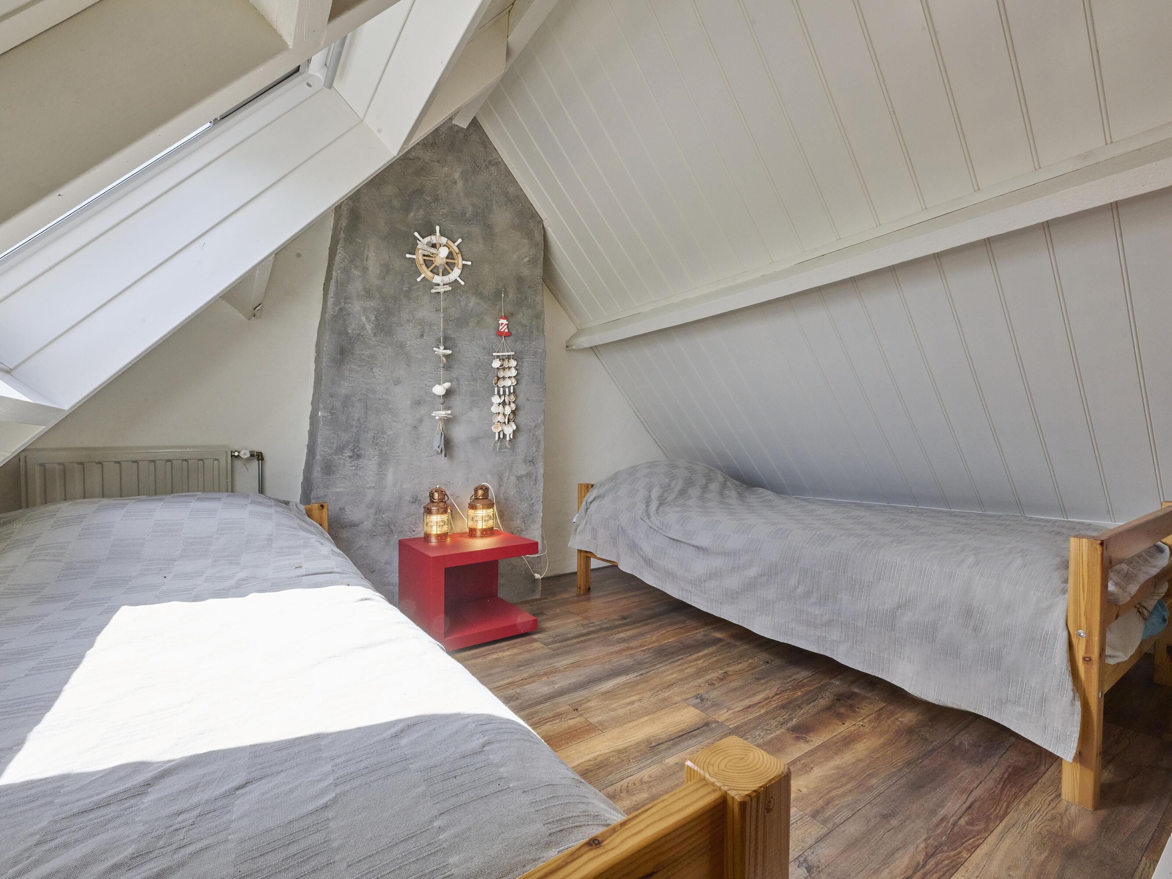 Ein Schlafzimmer im Loft-Stil mit zwei Betten, einem roten Nachttisch und einer Wanddekoration mit Schiffsschwengel und aufgehängten Muscheln.