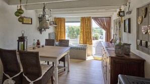 Ein Essbereich mit Holztisch und Korbstühlen, einem hängenden Laternen und Blick ins Freie durch ein Fenster mit Vorhängen.