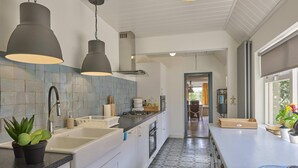 Eine moderne Küche mit weißen Schränken, einer schwarzen Arbeitsplatte und einer gemusterten Spritzschutzwand. Es gibt ein Spülbecken mit Armatur, einen Herd und Deckenleuchten.