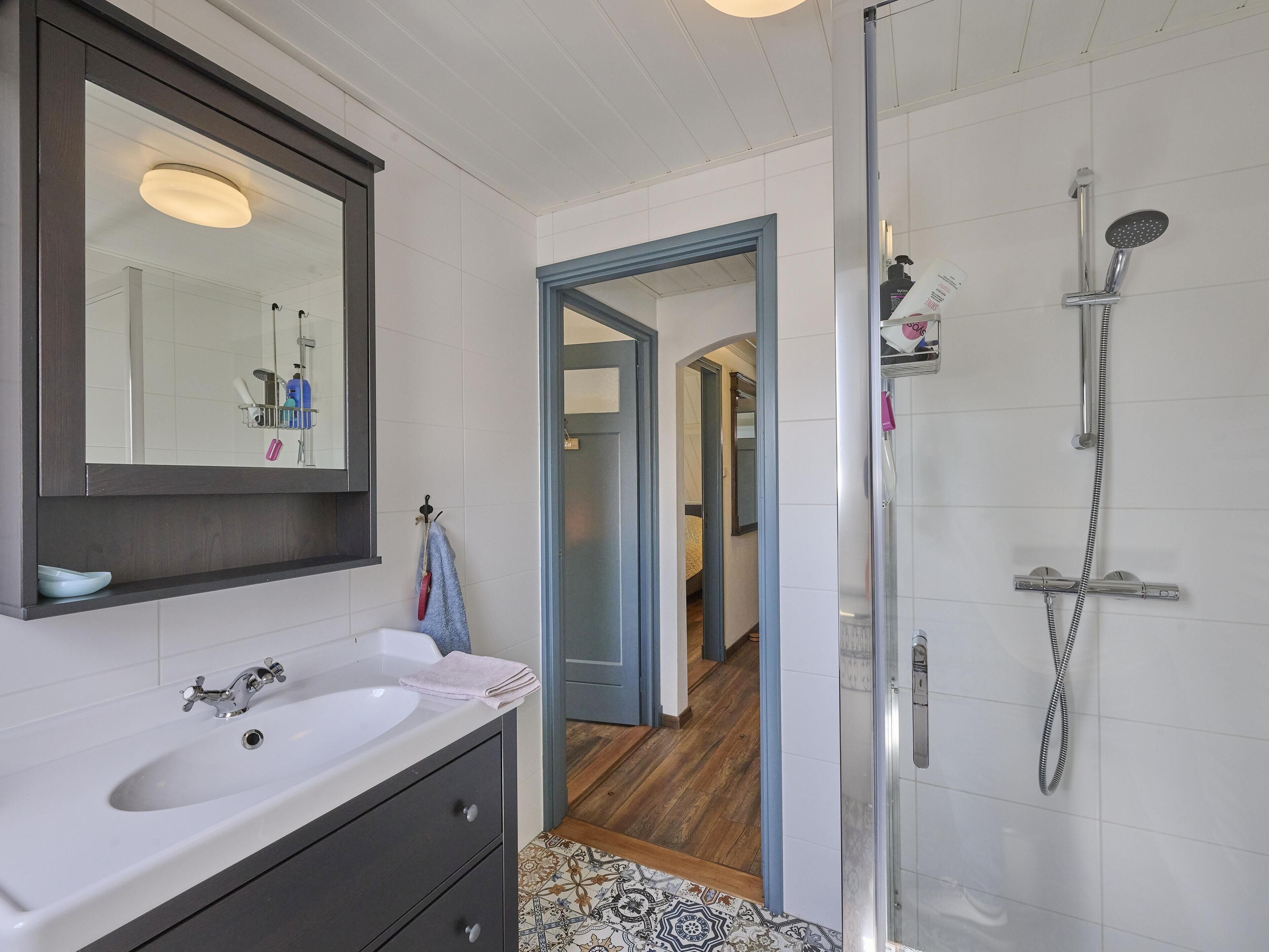 Une salle de bain moderne avec un lavabo blanc, un meuble-lavabo foncé et une cabine de douche en verre.
