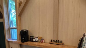 A wooden bar area with a coffee maker, jars, and bottles on a shelf. There are two stools and a trash bin. - Unique Cortes Treehouse! - Peaceful haven in the trees (Strathcona B)