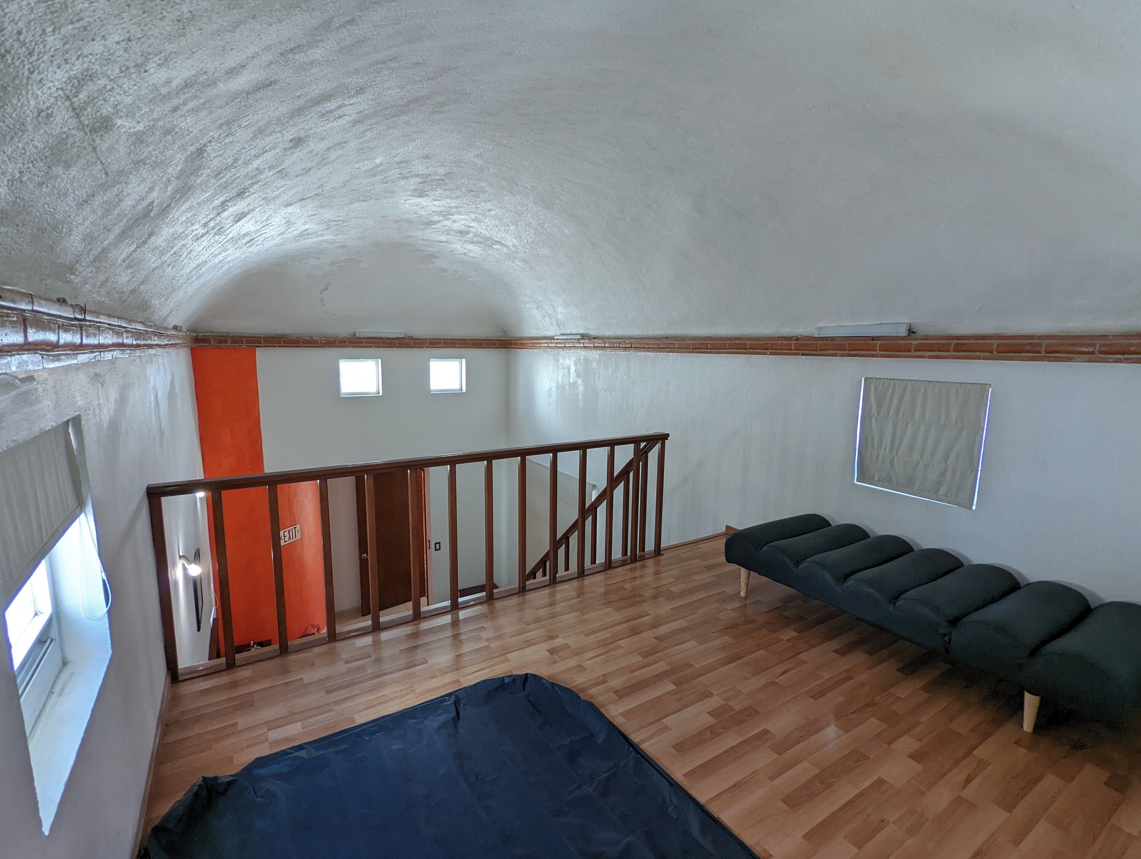 A room with a sloped ceiling, wooden flooring, a staircase, a sofa, and a door marked "EXIT".
