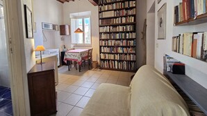Un salon confortable avec un canapé, une table à manger et des chaises, un coin cuisine avec une cuisinière et une grande bibliothèque remplie de livres.