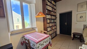 Une pièce chaleureuse comprenant une table à manger, des chaises, une bibliothèque et une fenêtre donnant sur les bâtiments environnants.