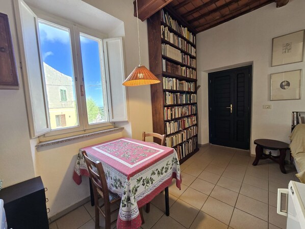 A cozy room with a dining table, chairs, a bookshelf, and a window with a view of buildings outside.