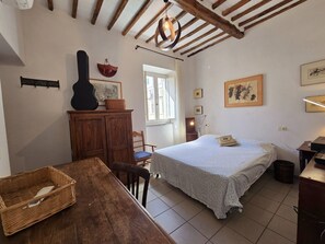 A cozy bedroom with a bed, a wooden dresser, a dining table, and a guitar.