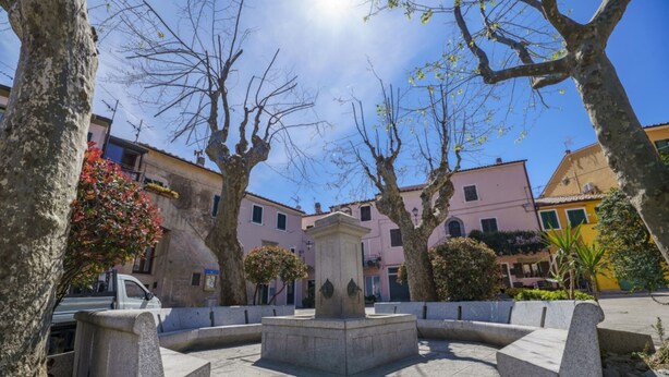 Une cour intérieure avec une fontaine centrale, entourée de bancs en pierre et d’arbres.