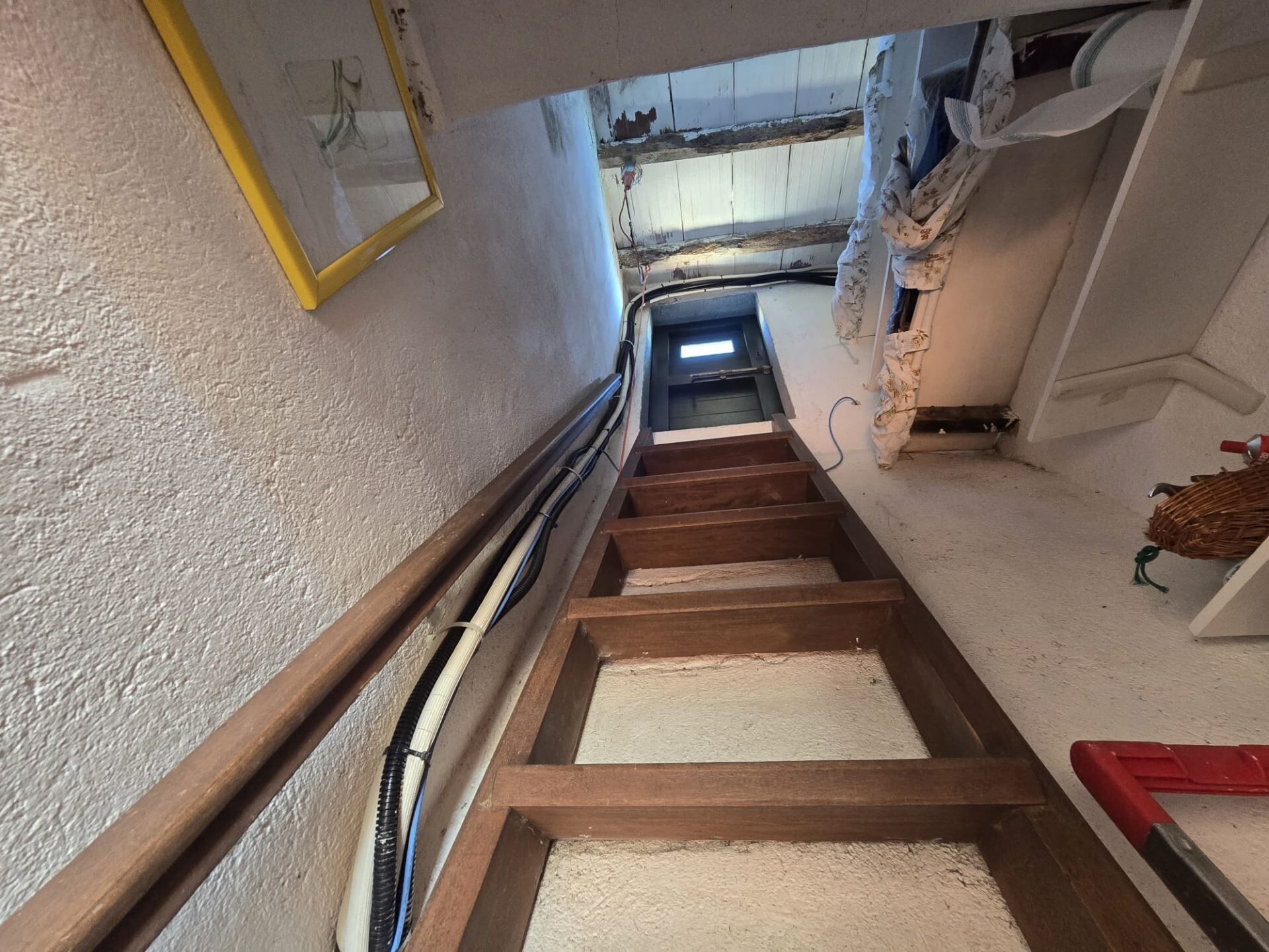 A narrow stairway with wooden steps and a metal handrail, leading to a door at the top.