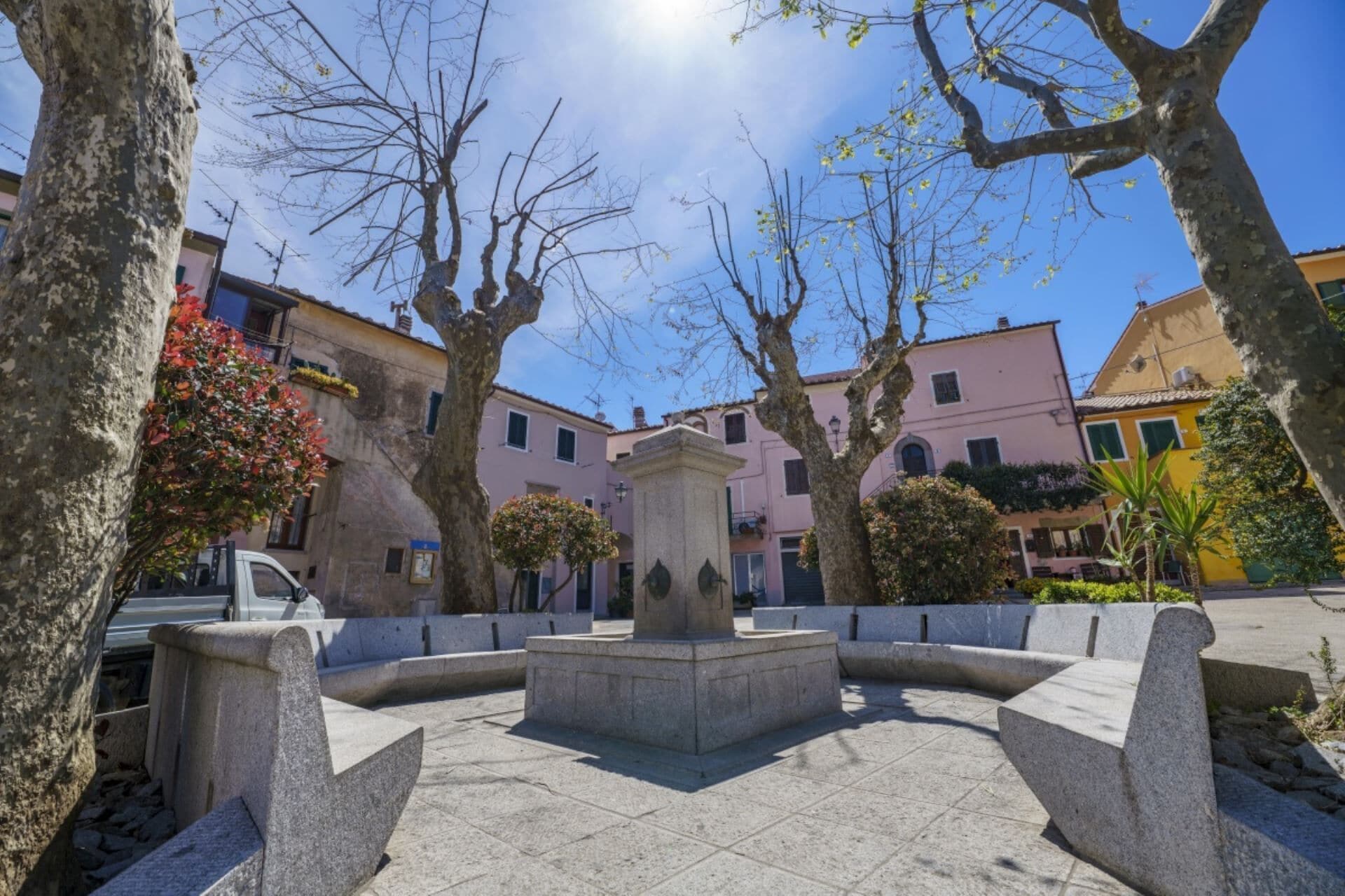 Une cour intérieure avec une fontaine centrale, entourée de bancs en pierre et d’arbres.