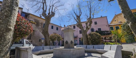 Une cour intérieure avec une fontaine centrale, entourée de bancs en pierre et d’arbres.