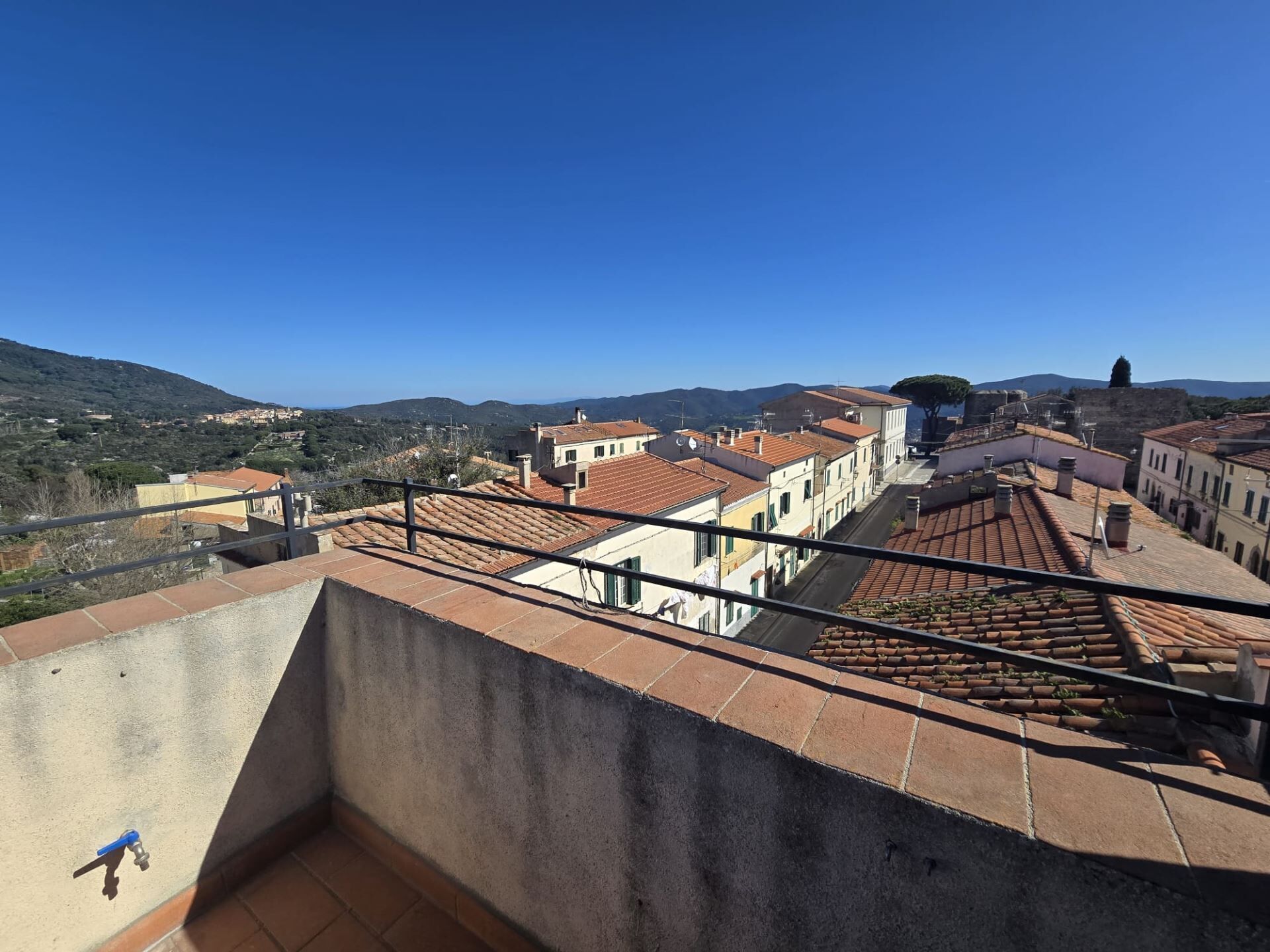 Une terrasse sur le toit offrant une vue sur la ville, avec des bâtiments aux toits de tuiles et une chaîne de montagnes lointaine.