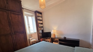 Une chambre à coucher avec un lit, une bibliothèque, un bureau avec une lampe et un téléviseur.