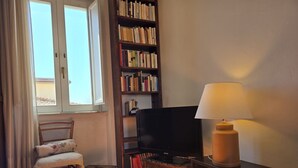 Une pièce comprenant un lit, une chaise, une bibliothèque, un téléviseur et une lampe.