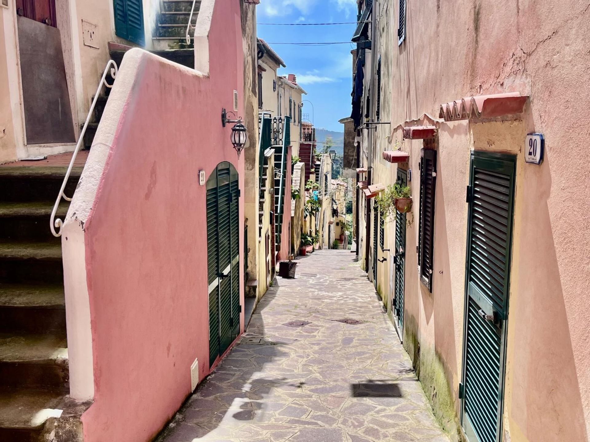 Un carrer estret amb edificis a ambdós costats, una escala a l'esquerra i un senyal de carrer que indica el número 90.