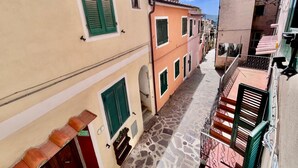 A narrow street with buildings featuring traditional architecture, including shuttered windows and stone-paved ground.