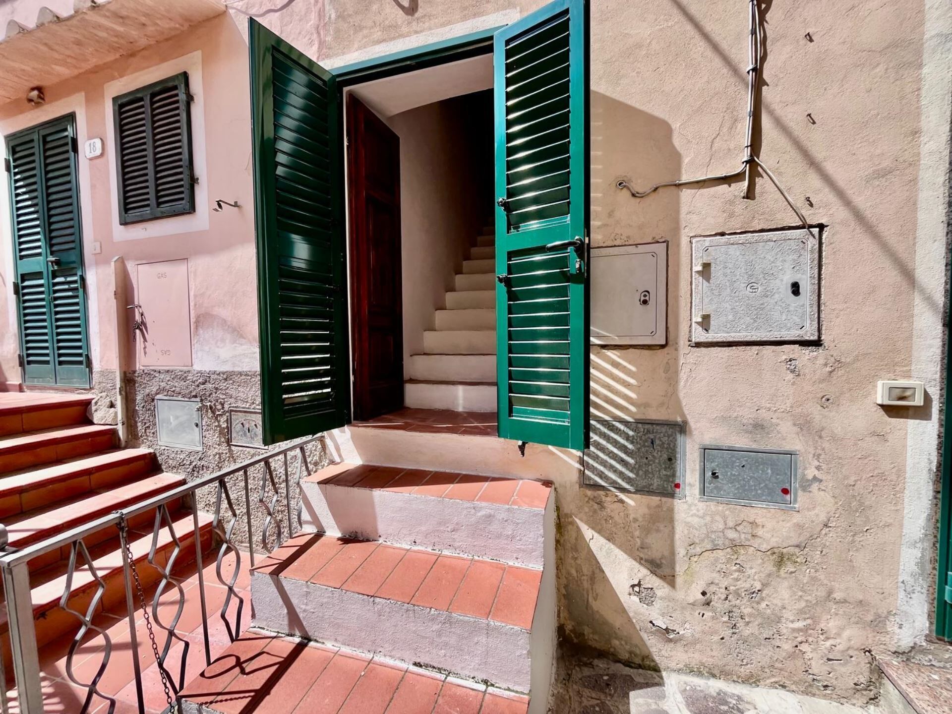 A staircase leading to a building entrance with green shutters, a metal railing, and a tiled floor.