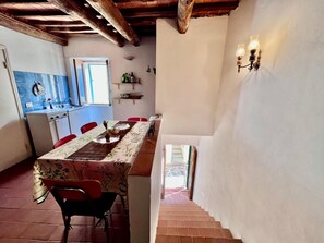 Uma sala de jantar com mesa posta para quatro pessoas, cozinha ao fundo e escada que leva a um andar superior.