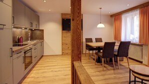 Ett modernt kök med trägolv, en matplats med bord och stolar samt ett stort fönster med gardiner.