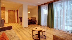 A modern living room with a wooden floor, a sofa, a round table, and a dining area with chairs. - Apartment 3 for 4 persons, 1 separate bedroom, balcony, 53 m² (Inzell)
