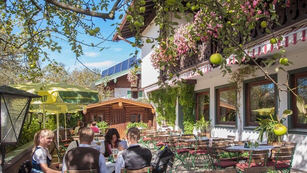 An outdoor café with tables and chairs, surrounded by greenery and a building with a balcony. - Apartment 3 for 4 persons, 1 separate bedroom, balcony, 53 m² (Inzell)